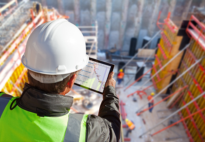 Civil engineer or architect with hardhat on construction site checking schedule on tablet computer